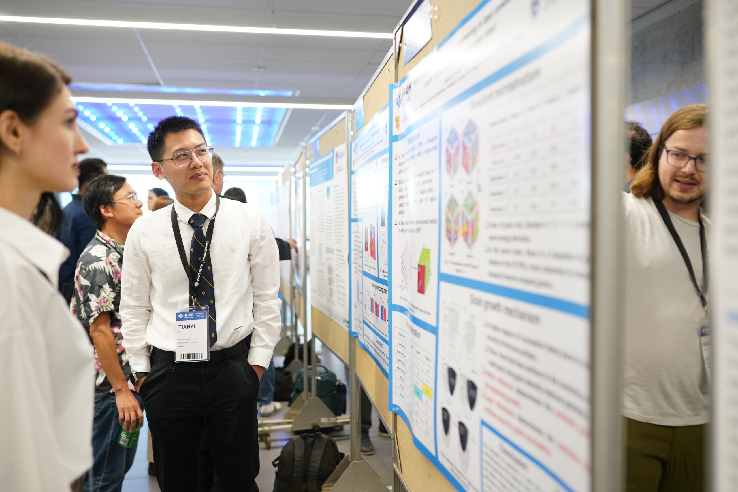 Conference attendees viewing and discussing research posters displayed on boards in a large hall.