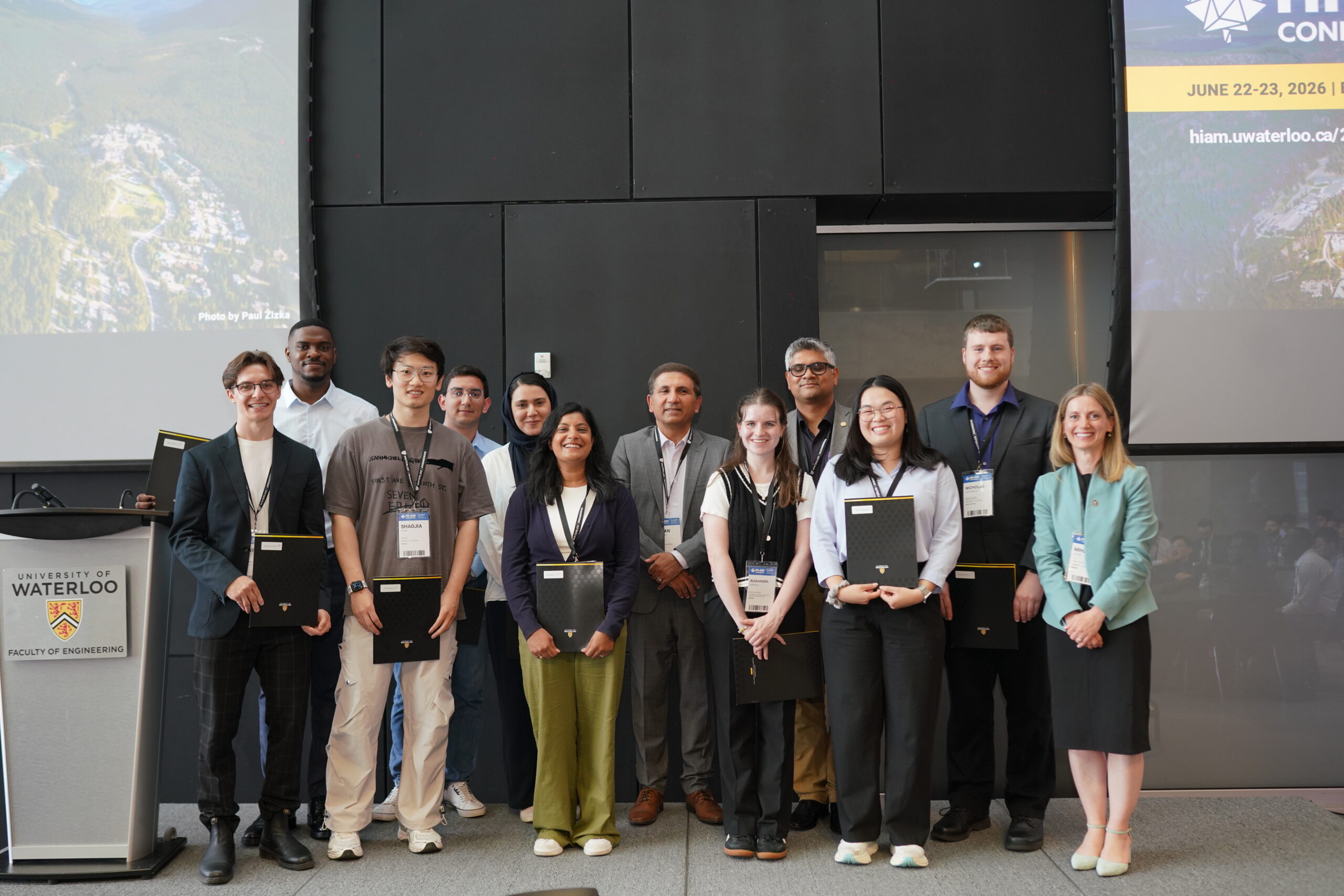 Group photo of award recipients standing beside the conference chairs, all smiling at the camera.